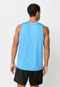 Jasnoniebieski sportowy top na ramiączkach, wykonany z oddychającego materiału, o luźnym kroju z detalem metki z tyłu. W połączeniu z czarnymi szortami.