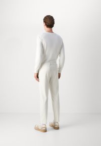 White knit sweater and matching tapered pants, both made of soft fabric. Light-colored sneakers accent the outfit with a textured sole.