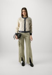 Giacca corta in morbido pelliccia finta bianca e nera, con polsini elasticizzati. Pantaloni cargo larghi verde oliva con zip e tasche. Borsa nera e stivali alla caviglia.