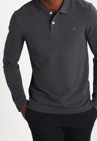 Långärmad, mörkgrå polo-shirt i strukturerad tyg, med en vanlig krage, tre knappar och en liten logotyp på bröstet.