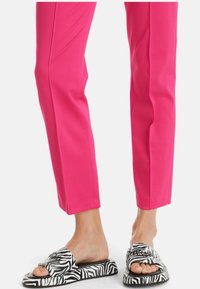 Pantalons ajustés fuchsia associés à des sandales à enfiler à imprimé zèbre noir et blanc, dotées d'une semelle plate et d'un design ouvert à l'avant.