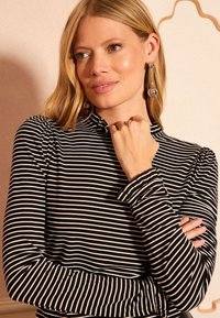 Fekete-fehér csíkos hosszú ujjú felső fodros gallérral és testhez álló ujjal. Az anyag puhanak és rugalmasnak tűnik.