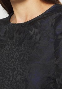 Černá vzorovaná látka s texturovaným povrchem, s kulatým výstřihem a sofistikovaným designem, vhodná pro formální příležitosti.