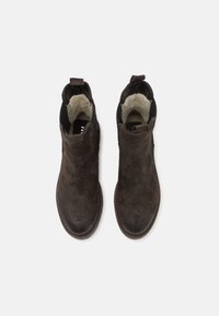 Bottines en suede marron foncé avec un bout arrondi, une doublure intérieure douce, des panneaux latéraux élastiques et une languette au talon pour un enfilage facile.