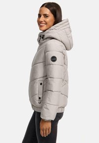 Svijetlosiva puffer jakna s kapuljačom, koja ima kvadratne dijelove, oznaku logo na ruci i džepove sa preklopima na dugmad.
