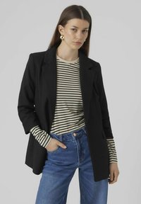 Blazer noir au design structuré, associé à une chemise à rayures beige et noire à manches longues, et un jean en denim bleu taille haute.
