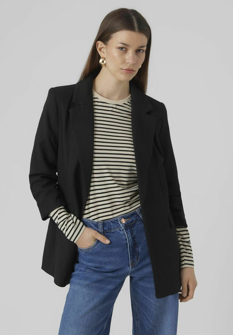 Blazer noir au design structuré, associé à une chemise à rayures beige et noire à manches longues, et un jean en denim bleu taille haute.