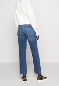 Höga blå denimjeans med rak ben, urblekt textur, femficksdesign och fransad fåll. Matchas med mönstrade slip-on skor.