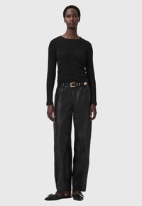 Zwart langetermijn top met een gestructureerd breipatroon, gecombineerd met losse zwarte leren broek. Geaccessoriseerd met een gouden riem en platte schoenen.