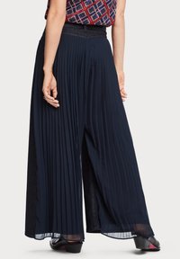 Pantalons larges plissés bleu marine avec une taille texturée, en tissu léger et semi-transparent, et avec des fentes latérales pour plus de liberté de mouvement.