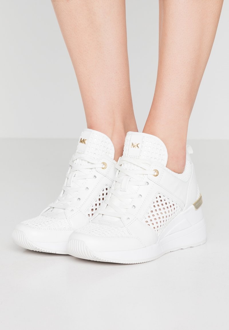 Sneakers sportivi bianchi con dettagli in rete, accenti dorati e tacco a zeppa. Scamosciato sintetico testurizzato e design della suola a contrasto.