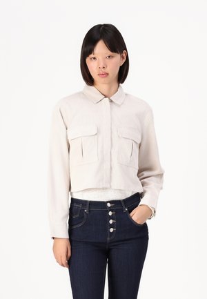 Lichtbeige cropped shirt met een kraag, twee zakflappen en lange mouwen, gecombineerd met donkerblauwe high-waisted jeans met knoopsluiting.