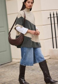Knitted poncho in beige and dark gray stripes, paired with wide denim culottes and knee-high brown leather boots. Brown shoulder bag.