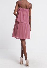 Rosa, gestuftes Kleid mit dünnen Trägern, das eine transparente obere Schicht und eine feste untere Schicht aufweist, kombiniert mit hellen High Heels.
