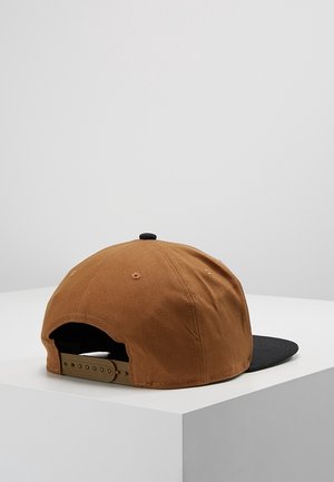 Brun snapback kasket med sort skygge liggende på en hvid overflade, der viser den justerbare rem bagpå.