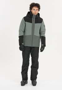 Sne jacket i grøn og sort med lynlås foran, hætte og elastiske manchetter. Sæt sammen med sorte bukser og handsker, alt sammen velegnet til vintersport.