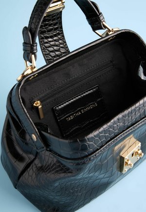 Schwarze Handtasche aus Krokodilleder mit Prägung und goldenen Beschlägen, ausgestattet mit einer Reißverschlusstasche und einem markierten Innenlabel, von oben betrachtet.