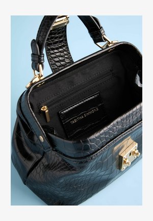 Juodas aligatorius efekto odinis rankinės su auksinėmis detalėmis, turinti užtrauktuku užsegamą kišenę ir prekės ženklo interjero etikete, rodoma iš viršaus.