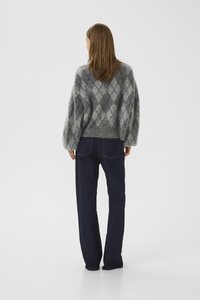 Woman standing facing away, wearing a gray argyle patterned sweater and dark blue straight-leg jeans on a plain light background.