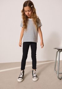 Camiseta de algodón de manga corta a rayas en blanco y azul marino, combinada con jeans negros ajustados y zapatillas altas negras con cordones blancos.