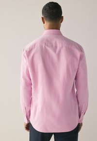 Svijetlo ružičasta košulja dugih rukava izrađena od tkanog materijala; ima ovratnik s dugmadi i jedan gumb na manžetama; glatke teksture.