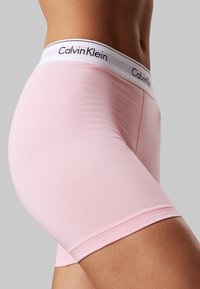 Calvin Klein ružičasti pamučni bokserice s bijelim pojasom na kojem su crna slova. Glatka tekstura s uskim dizajnom i dužinom do sredine bedara.