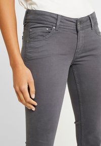 Šedé džíny slim fit, vyrobené z měkké bavlněné tkaniny. Obsahují pět kapes, kovové detaily a viditelné švy podél švů.