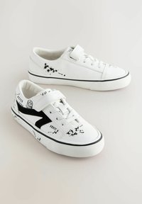 Białe sneakersy mają teksturowaną gumową podeszwę, zapięcie na sznurowadła i rzep, czarny nadruk w plamy oraz boczne akcenty z czystego tekstylu.