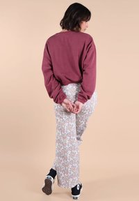 Sweatshirt oversized bordeaux à manches longues, associé à un pantalon clair à motifs floraux. Des baskets noir et blanc apportent du contraste.