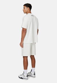 Set di t-shirt oversized in cotone bianco e pantaloni corti, caratterizzato da una vestibilità ampia e dettagli di cucitura a contrasto. Abbinato a sneakers grigie e bianche.