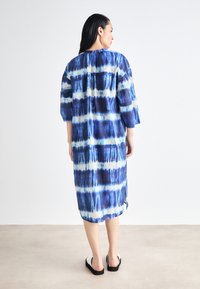 Rochie lungă, cu croială lejeră, având modele tie-dye albastre și albe, mâneci până la trei sferturi și o margine despicată pentru un plus de detaliu.