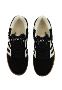 Un paio di sneakers bianche e nere con tessuto testurizzato, lacci neri e suole in gomma color nocciola, viste dall'alto su uno sfondo bianco.