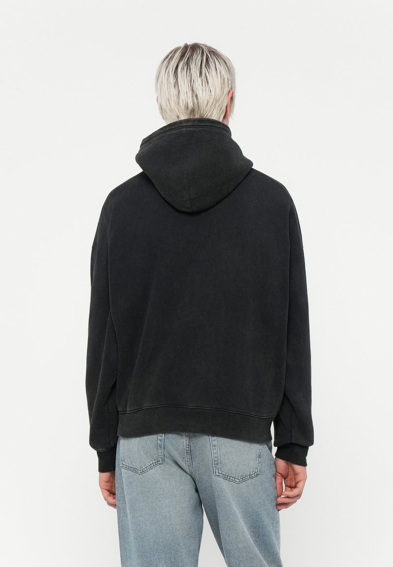 Felpa nera oversize con un grande cappuccio, polsini e orlo a costine. Indossata con jeans in denim azzurro chiaro, tessuto testurizzato e design casual.