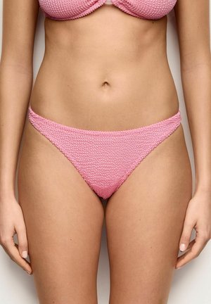Kobieta w różowym teksturowanym dołu od bikini i pasującym topie, pokazana od talii do górnej części ud na gładkim tle.