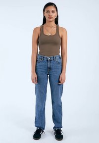 Hnědý trikotový top s žebrovanou strukturou a modré džíny s vysokým pasem. Džíny mají klasický střih, pět kapes a jsou vyrobeny z denimu. Oblečení doplňují černé tenisky.