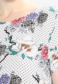 Floral-patterned top with a white background and black polka dots. Features colorful flowers in red, purple, and green. Lightweight fabric, relaxed fit.