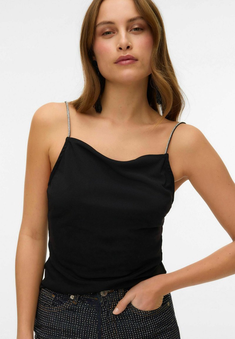 Sort camisole med et draperet halsudskæring og tynde, perlebesatte spaghettistropper, parret med mørke denim med sølvdetaljer.