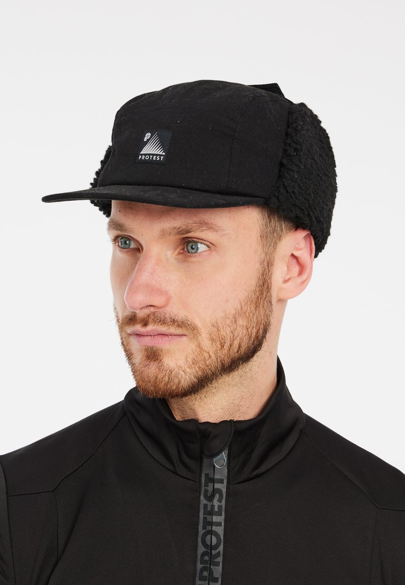 Black cap with a soft, textured earflap design. Features a front logo patch and a slightly curved visor. Suitable for cold conditions.