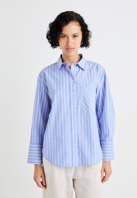 Camicia a righe blu e bianche con chiusura a bottoni, colletto e taschino singolo; presenta maniche lunghe con accenti a righe.