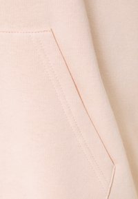 Primer plano de una tela de color rosa claro que presenta una costura plana y un detalle de bolsillo en ángulo.