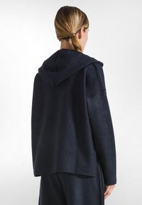 Marinblå hoodie med en mjuk, texturerad yta. Har en stor huva och en avslappnad passform, med en asymmetrisk nederkant och minimal sömdetalj.