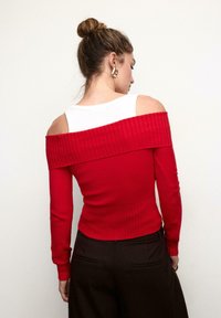 Roter, gerippter Pullover mit Carmenausschnitt und langen Ärmeln, mit einem weißen Baumwoll-Unterziehshirt-Design. Glatte Textur, figurbetonter Stil.