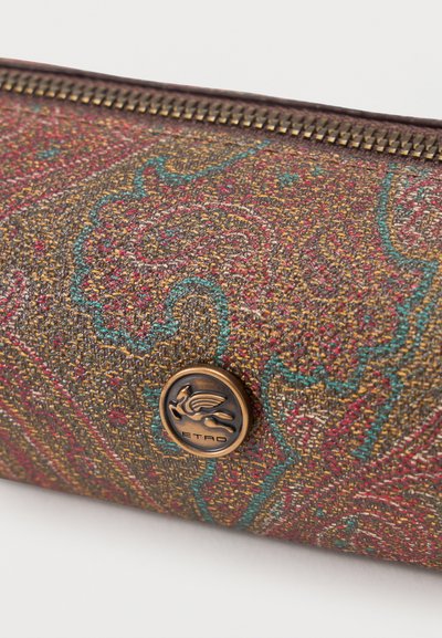 Close-up of a textured fabric pouch with multicolored paisley pattern and a bronze circle logo featuring a winged horse and "ETRO" text.