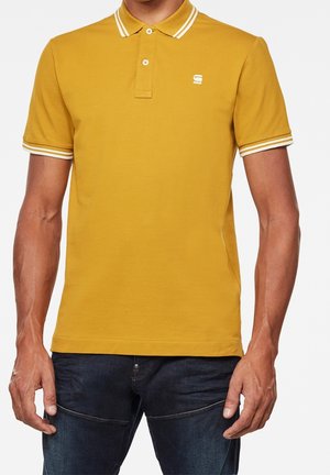 Żółta koszulka polo z kołnierzykiem i mankietami na rękawach w białe paski. Posiada dwuklamrowy dekolt i małe logo na piersi. Wykonana z bawełny.