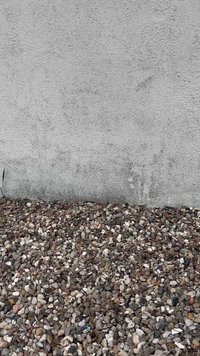 Mur en béton au-dessus d’un sol recouvert d’une couche de petits cailloux multicolores.