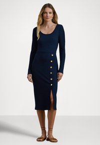 Marineblå ribbestrikket kjole med lange ermer, rund hals, sidesplitt og dekorative gullknapper på venstre side.