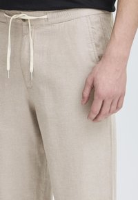 Pohodlné kalhoty z béžové lněné směsi s elastickým pasem na šňůrku, bočními kapsami a uvolněným střihem. Hladká textura a minimalistický design.