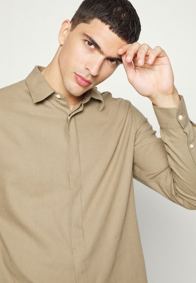 Camisa azul clara de manga longa com colarinho, fechamento frontal com botões e uma textura subtil. Apresenta punhos com botões e um corte descontraído.