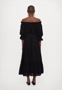 Črna off-the-shoulder obleka z nabrano blazino in robom, textured tkanina, srednje dolga, z pasom, nošena z ravnimi čevlji.