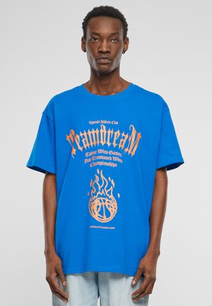 Blå bomulds t-shirt med oversized pasform, der har orange grafisk tekst og ild design. Korte ærmer og rund halsudskæring.
